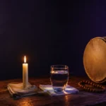 Vela, copo de água e atabaque sobre mesa de madeira, representando a diferença entre umbanda, espiritismo e catolicismo