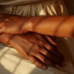 Maos em repouso com luz dourada sobre a pele, sobre sinais espirituais no corpo