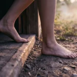 Pés descalços saindo de um piso de madeira para um caminho de terra ao amanhecer
