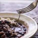 Fio de cabelo comprido puxado com o garfo de um prato de arroz e feijão sobre a mesa