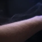 Antebraço em luz suave com arrepio na pele e leves rastros de luz ao redor