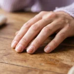 Mancha branca pequena na unha do dedo anelar de uma mão feminina apoiada sobre a mesa