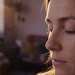 Mulher de perfil com o olho direito se fechando na luz do fim de tarde