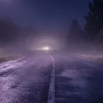 Estrada molhada à noite com faróis distantes na neblina, imagem simbólica do sonho com acidente de carro